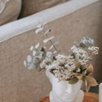 Cozy Living. - Cozy sofa with decorative cushions near stump with books and blooming flowers in vase in house room