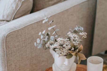 Cozy Living. - Cozy sofa with decorative cushions near stump with books and blooming flowers in vase in house room