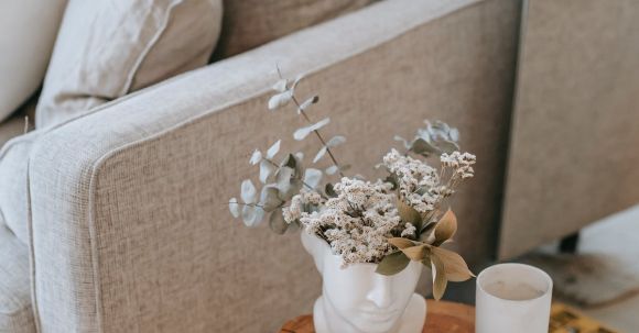 Cozy Living. - Cozy sofa with decorative cushions near stump with books and blooming flowers in vase in house room