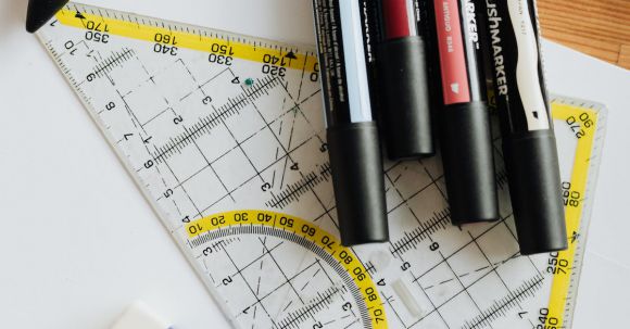 Color Scheme. - Top view of various markers and plastic drawing triangle with marked lines and numbers placed on blank paper near eraser on wooden table in office