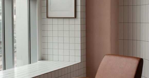 Small Space Decor Ideas - Blank frame hanging on tiled wall near window in small light room with soft brown leather armchair on floor at home
