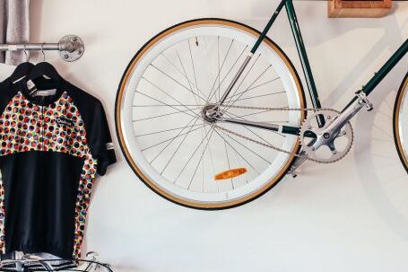 Stylish Storage. - Bicycles at white wall with various t shirts hanging on hangers on metal racks in light room with transport in storage