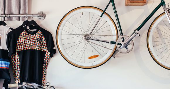 Stylish Storage. - Bicycles at white wall with various t shirts hanging on hangers on metal racks in light room with transport in storage