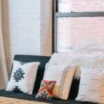 Interior Design - Light room interior with decorative cushions on soft couch against fabric bench on parquet at home
