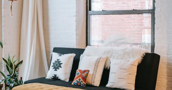 Interior Design - Light room interior with decorative cushions on soft couch against fabric bench on parquet at home