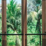 Luxury Properties - Wooden chair placed in spacious villa near panoramic windows overlooking lush green tropical garden against cloudless blue sky
