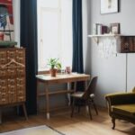 Interior Design - Comfortable couch put on wooden floor covered with rug and potted plants in apartment with big windows and dark curtains in sunlight