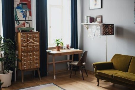 Interior Design - Comfortable couch put on wooden floor covered with rug and potted plants in apartment with big windows and dark curtains in sunlight