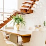 Interior Design - Minimalistic design of spacious room with second level space and wooden staircase against large windows in modern house in daytime