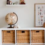 Interior Design - Comfortable bed with toys globe and paintings placed on wooden cabinet with wicker boxes and soft white rug with toy house on floor