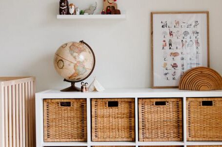 Interior Design - Comfortable bed with toys globe and paintings placed on wooden cabinet with wicker boxes and soft white rug with toy house on floor