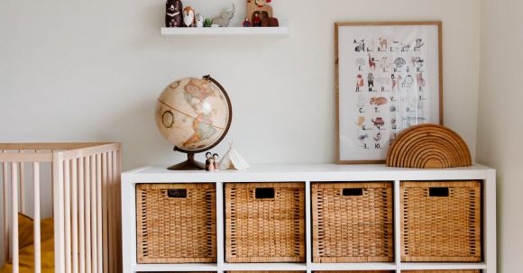 Interior Design - Comfortable bed with toys globe and paintings placed on wooden cabinet with wicker boxes and soft white rug with toy house on floor