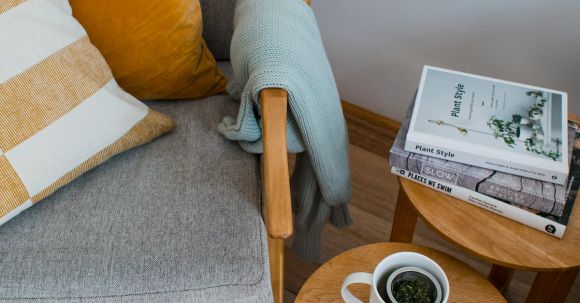 Interior Design - From above of comfortable armchair with colorful pillows placed near wooden side tables with books and cup of tea in living room