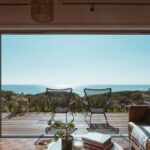 Luxury Properties - Interior design of luxurious apartment with large balcony doors and wooden terrace having picturesque view on green forested seashore and calm blue sea