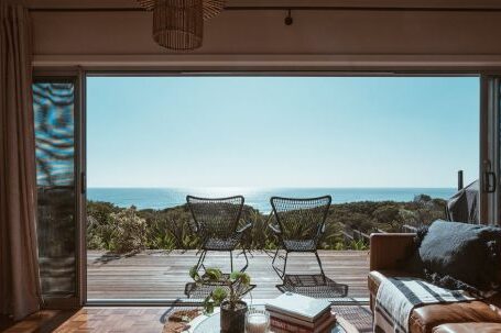 Luxury Properties - Interior design of luxurious apartment with large balcony doors and wooden terrace having picturesque view on green forested seashore and calm blue sea