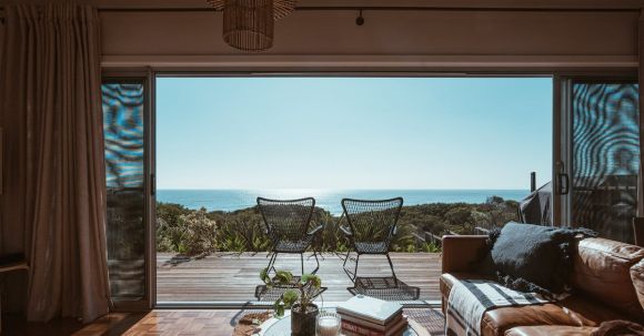 Luxury Properties - Interior design of luxurious apartment with large balcony doors and wooden terrace having picturesque view on green forested seashore and calm blue sea