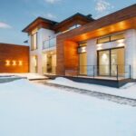 Luxury Properties - Exterior architecture of private suburban cottage house with stone and wooden facade and large windows overlooking spacious snow covered yard in winter day