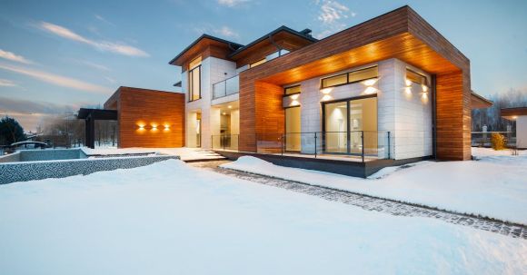 Luxury Properties - Exterior architecture of private suburban cottage house with stone and wooden facade and large windows overlooking spacious snow covered yard in winter day