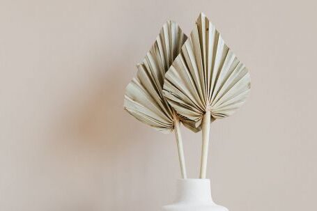 Unique Furniture - Decorative golden leaves in unique formed white vase placed on marble table against beige background