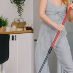 Housewife Washing Floor - Young carefree female in jumpsuit dancing while cleaning parquet with mop in light house room