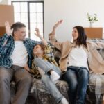 New Home - Happy Family Sitting on the Couch Covered with Plastic