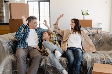 New Home - Happy Family Sitting on the Couch Covered with Plastic