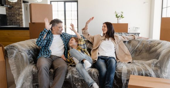 New Home - Happy Family Sitting on the Couch Covered with Plastic