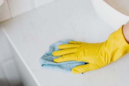 Bathroom Vanity - From above crop unrecognizable person with microfiber cloth wearing yellow rubber glove and cleaning white marble tabletop of vanity table with washbasin in bathroom