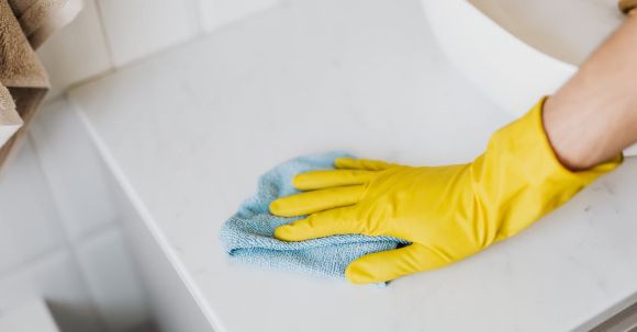 Bathroom Vanity - From above crop unrecognizable person with microfiber cloth wearing yellow rubber glove and cleaning white marble tabletop of vanity table with washbasin in bathroom