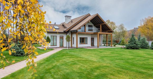 Luxury Properties - Exterior of residential suburban cottage with balcony surrounded with lush green plants and trees