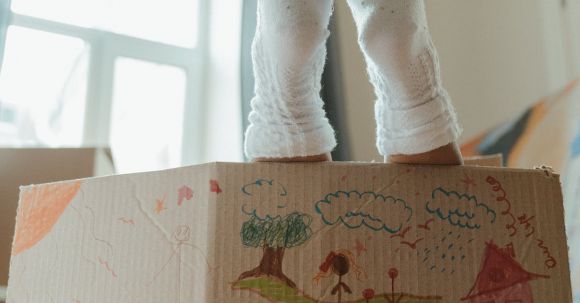New Home - Person in White Pants and White Socks Standing Beside Brown Cardboard Box