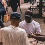 Neighborhood - Men Sitting Beside Table on Pathway Near People Walking Beside Rail