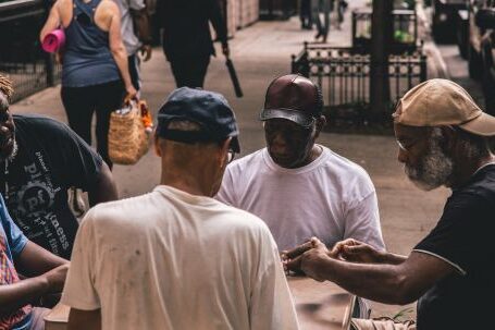 Neighborhood - Men Sitting Beside Table on Pathway Near People Walking Beside Rail