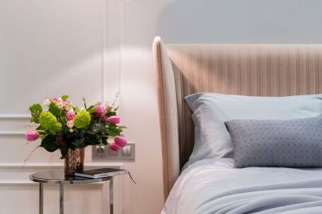 Luxury Properties - Interior of modern light bedroom with pillows and blanket on bed near round table with bouquet of flowers in vase under lamps