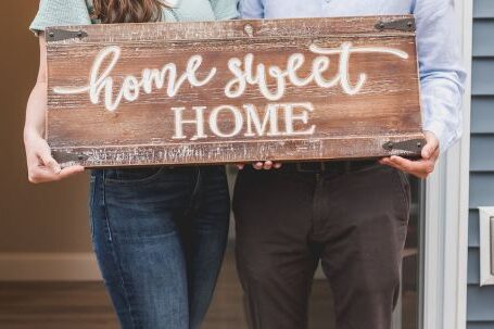 New Home - Happy Couple Standing Face to Face and Holding a Home Sweet Home Wooden Signage