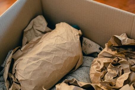 Craft Packaging - From above of open cardboard box on wooden floor full of things wrapped in packaging paper prepared for moving in new apartment