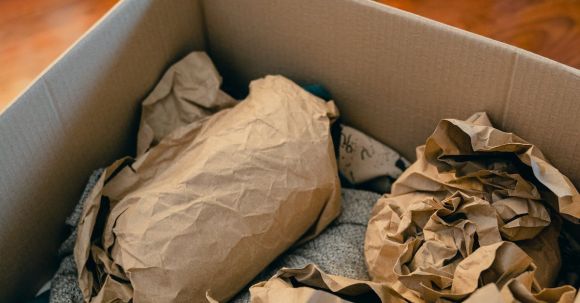 Craft Packaging - From above of open cardboard box on wooden floor full of things wrapped in packaging paper prepared for moving in new apartment