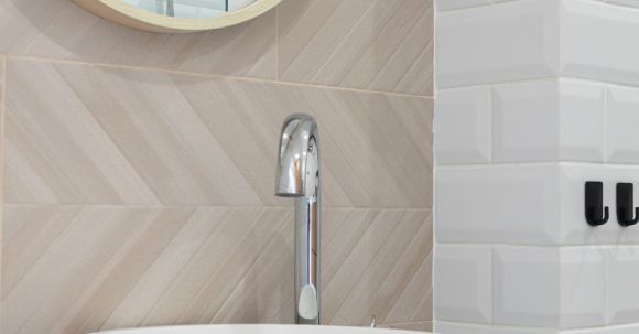 Luxury Properties - Interior of light modern restroom with sink and faucet on cabinet under mirror on tile wall