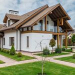 Luxury Properties - Exterior of modern cottage house with columns and balcony surrounded by green grass and trees
