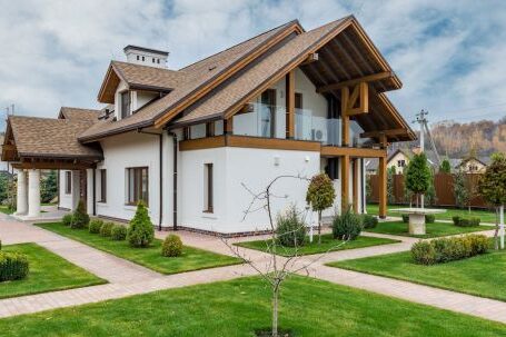 Luxury Properties - Exterior of modern cottage house with columns and balcony surrounded by green grass and trees