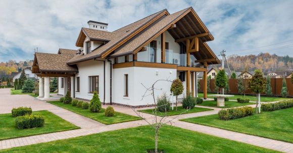 Luxury Properties - Exterior of modern cottage house with columns and balcony surrounded by green grass and trees